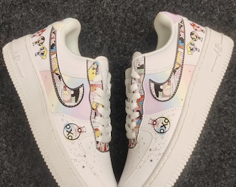 May include: Pair of white sneakers with cartoon character designs. The shoes feature a white sole, laces, and a colorful design on the sides and heel. The design includes a rainbow gradient and cartoon characters.