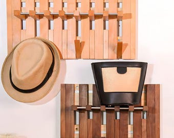 May include: Two wooden wall-mounted coat racks with a hat and a purse hanging on them. The top rack is light-colored wood, and the bottom rack is dark-colored wood. The hat is tan with a black band, and the purse is black with a tan front.