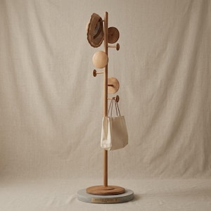 May include: A wooden coat rack with a round base, featuring multiple pegs and decorative wooden circles. A straw hat and a canvas tote bag hang from the rack. The rack is made of light-colored wood and stands on a concrete base.