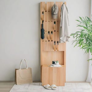 Può includere: Un attaccapanni in legno chiaro con una panca integrata. Un ombrello, un cappello e un asciugamano sono appesi all'attaccapanni. Una borsa, una fotocamera e delle pantofole sono nelle vicinanze. L'attaccapanni è fatto di doghe di legno verticali.
