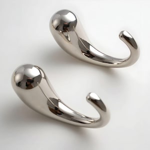 Puede incluir: Dos ganchos de pared de metal plateado pulido. Cada gancho tiene un cuerpo en forma de lágrima que se curva en un gancho redondeado. Los ganchos son reflectantes, con una superficie lisa y brillante. Los ganchos están diseñados para colgar objetos.