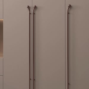 May include: Three long, vertical, dark brown metal cabinet handles attached to flat, matte taupe cabinet doors. Each handle features a smooth, slender rod design with a rounded, teardrop-shaped top finial, creating a clean and uniform appearance.