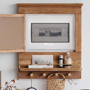 May include: A wooden wall shelf with a white electrical panel, a small picture frame, a book titled "Matches", two glass bottles, a small woven basket, and four gold hooks.