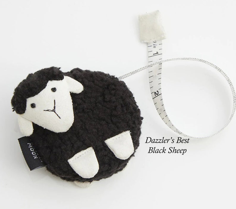 May include: A black sheep-shaped measuring tape with a white face and feet. The tape extends to 2 inches and is labeled "Dazzler's Best Black Sheep". The tape measure is a novelty item.