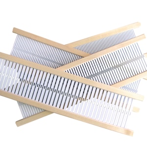 May include: Several small wooden weaving looms are stacked on a white background. Each loom has a light wood frame with white warp threads stretched across. The looms are designed for creating woven textiles and crafts.