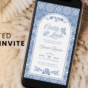 Może przedstawiać: Smartfon wyświetla zaproszenie na baby shower z niebiesko-białym kwiatowym wzorem. Zaproszenie brzmi "Cielito Lindo" i zawiera szczegóły wydarzenia. Telefon leży na teksturowanej powierzchni, z tekstem: "ANIMATED VIDEO INVITE" i "Canva".