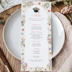 May include: A graduation party menu card with floral accents. The menu features appetizers, main courses, desserts, and drinks. The card is decorated with colorful flowers and a graduation cap illustration. The menu is placed on a white plate with silverware.