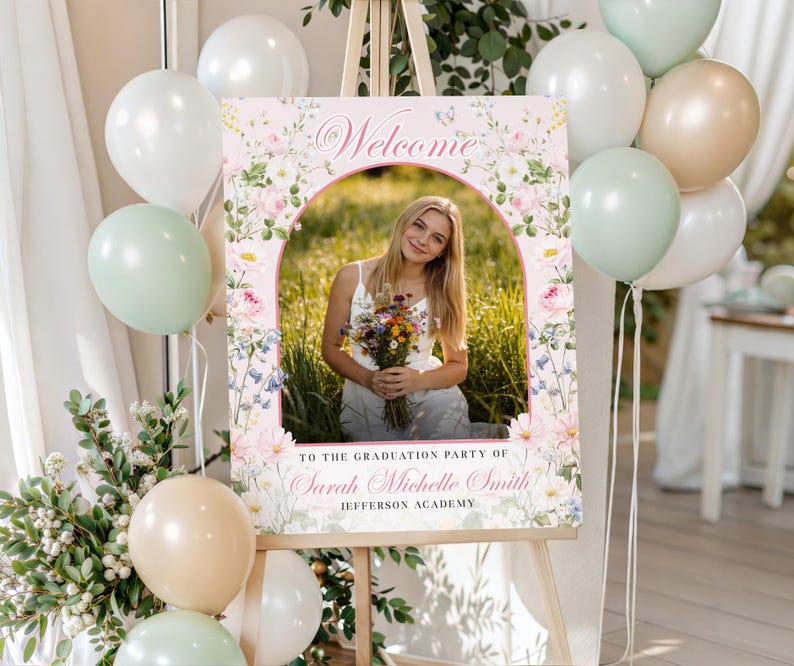 May include: A graduation welcome sign on an easel. The sign has a photo of a young woman with flowers, floral designs, and the word "Welcome". White, green, and tan balloons are arranged nearby. The sign is for Sarah Michelle Smith.
