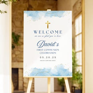 以下が含まれることがあります： 最初の聖体拝領のお祝いのための、青と金のウォーターカラーのウェルカムサイン。サインには、「ようこそ、お越しいただきありがとうございます。デイビッドの最初の聖体拝領のお祝い、05.20.25、イングリッシュタウン、ニュージャージー」と書いてあります。