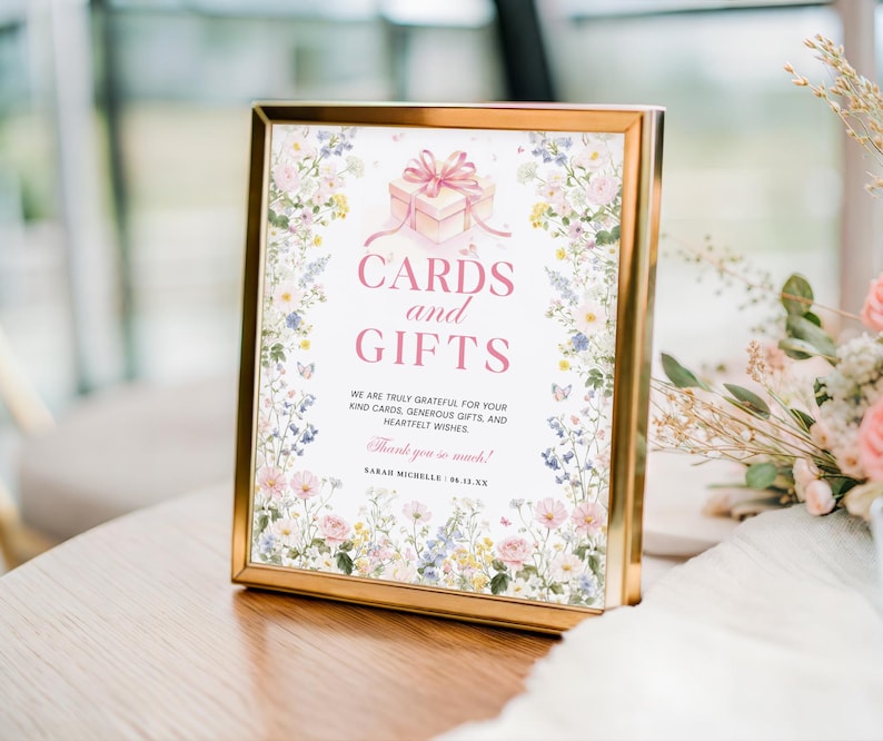 May include: A gold-framed sign with the text "CARDS and GIFTS" in pink. The sign features a floral border and a gift box illustration. The text reads "We are truly grateful for your kind cards, generous gifts, and heartfelt wishes."