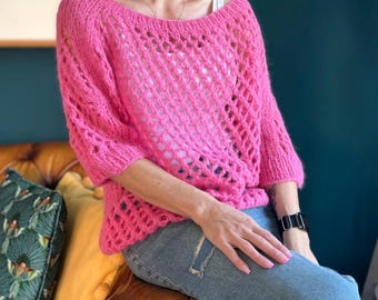 Può includere: Un maglione rosa lavorato a uncinetto con una vestibilità ampia e un delicato motivo traforato. Il maglione ha una scollatura ampia e maniche a tre quarti.
