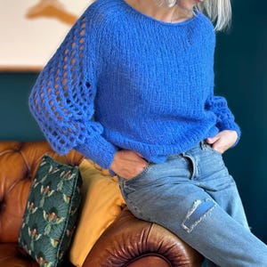 Peut inclure: Un pull en maille bleu flou avec des manches ajourées. Le pull est porté sur un jean bleu.