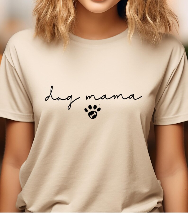 K&ouml;nnte beinhalten: Ein beiges T-Shirt mit dem Text "dog mama" in schwarzer Schrift und einem Pfotenabdruck mit einem Knochen darin.