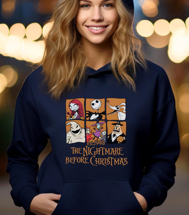 May include: Navy blue hooded sweatshirt featuring a graphic design of characters from "The Nightmare Before Christmas." The design includes images of Sally, Jack Skellington, and other characters. The text "EST.1993 THE NIGHTMARE BEFORE CHRISTMAS" is printed below the images.