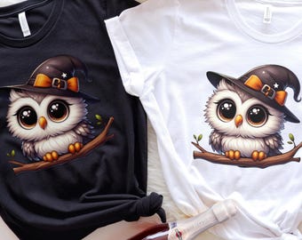 May include: Black and white t-shirts featuring a cartoon owl wearing a witch hat. The owl has large eyes and is perched on a branch. A bottle of rose wine is in the foreground.