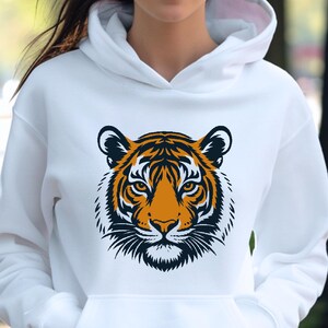 May include: White hoodie featuring a tiger face graphic. The tiger design is orange, black, and white, with detailed facial features. The hoodie has a drawstring hood and a front pocket.