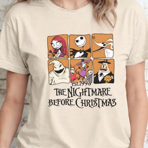 May include: Beige t-shirt featuring a graphic design from "The Nightmare Before Christmas." The design includes six character portraits in orange squares, the text "est.1993," and the film's title in black font.