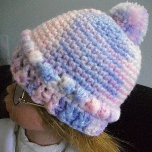 May include: A crocheted hat with a pink and blue ombre design and a fluffy white pom pom on top.