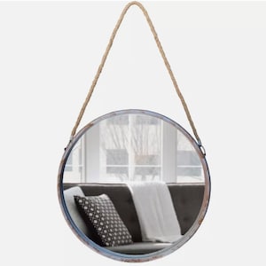 52cm diameter industrial style round mirror hanging on wall by its jute rope hanger, the frame is made from metal and finished in a rustic silver.