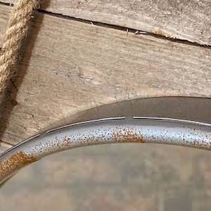 47cm diameter industrial style round mirror hanging on wall by its jute rope hanger, the frame is made from metal and finished in a rustic silver.