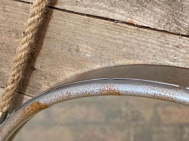 47cm diameter industrial style round mirror hanging on wall by its jute rope hanger, the frame is made from metal and finished in a rustic silver.