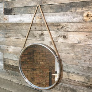 47cm diameter industrial style round mirror hanging on wall by its jute rope hanger, the frame is made from metal and finished in a rustic silver.