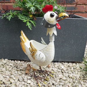May include: White metal chicken planter with a black and white polka dot bandana, red comb, and yellow feet. The planter has a white speckled finish and a yellow and brown design on the tail feathers.