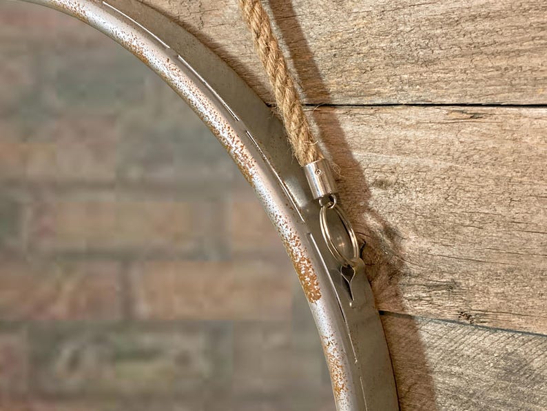 47cm diameter industrial style round mirror hanging on wall by its jute rope hanger, the frame is made from metal and finished in a rustic silver.
