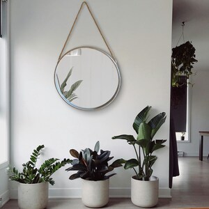 52cm diameter industrial style round mirror hanging on wall by its jute rope hanger, the frame is made from metal and finished in a rustic silver.