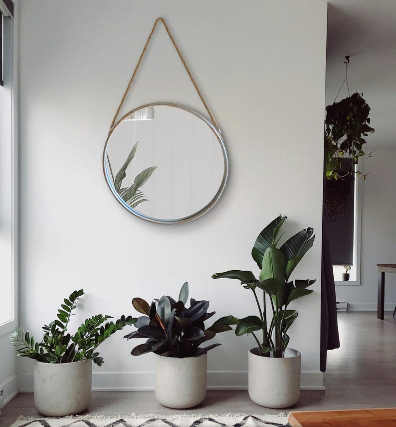 52cm diameter industrial style round mirror hanging on wall by its jute rope hanger, the frame is made from metal and finished in a rustic silver.