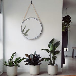 47cm diameter industrial style round mirror hanging on wall by its jute rope hanger, the frame is made from metal and finished in a rustic silver.