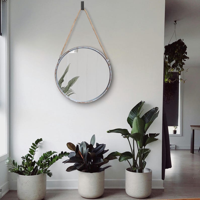 47cm diameter industrial style round mirror hanging on wall by its jute rope hanger, the frame is made from metal and finished in a rustic silver.