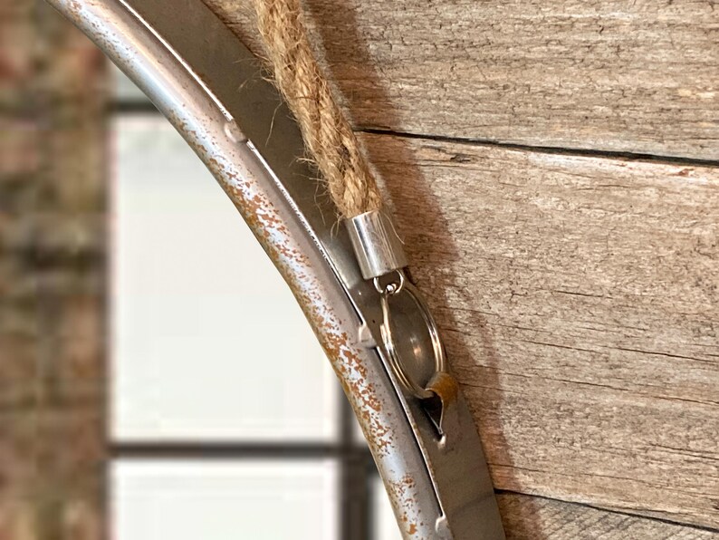 52cm diameter industrial style round mirror hanging on wall by its jute rope hanger, the frame is made from metal and finished in a rustic silver.