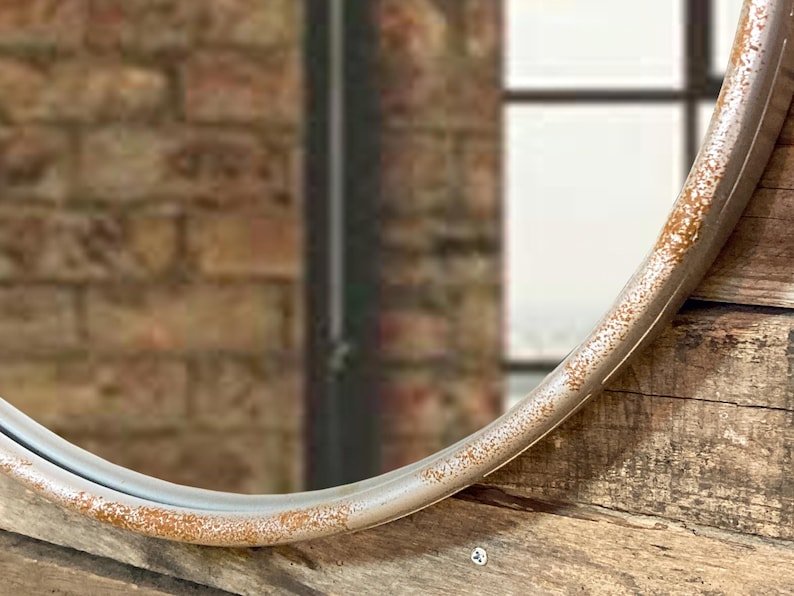 47cm diameter industrial style round mirror hanging on wall by its jute rope hanger, the frame is made from metal and finished in a rustic silver.