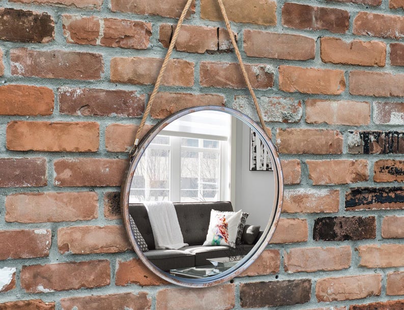 47cm diameter industrial style round mirror hanging on wall by its jute rope hanger, the frame is made from metal and finished in a rustic silver.