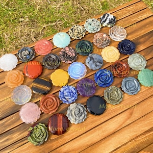 Op de afbeelding: Een verzameling gesneden edelsteenrozen in verschillende kleuren, waaronder wit, rood, blauw en groen. De rozen zijn gerangschikt op een houten oppervlak, waarbij de natuurlijke variaties en texturen van de stenen worden benadrukt. De afbeelding is goed belicht.