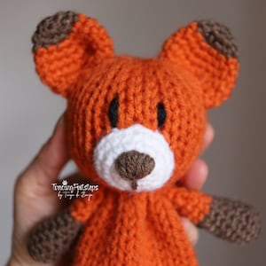 May include: A handmade orange fox plush toy with brown accents on the ears and paws. The fox has a white muzzle, black eyes, and a brown nose. The toy is knitted and appears soft.