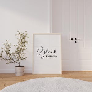 May include: A framed print with the word "Glück" in cursive script, followed by the words "Du. Ich. Wir." in a smaller font.