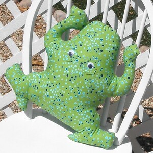 May include: A handmade green fabric monster pillow with blue and black polka dots. The pillow has two googly eyes and is sitting on a white chair. The monster has arms and legs.
