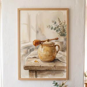 Pode incluir: Uma pintura em aguarela emoldurada representando um pote de mel dourado com uma colher de pau sobre a tampa. A cena inclui uma caneca branca e um pequeno ramo de vegetação, tudo sobre uma mesa de madeira rústica perto de uma janela.