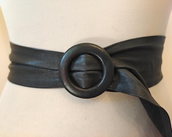 Puede incluir: Un cinturón de cuero negro con una hebilla grande, redonda y negra. El cinturón está envuelto alrededor de la cintura de un maniquí y atado en un nudo en el lateral.