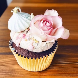 May include: A chocolate cupcake topped with a white frosting and sprinkles, decorated with a pink rose and a light blue meringue.
