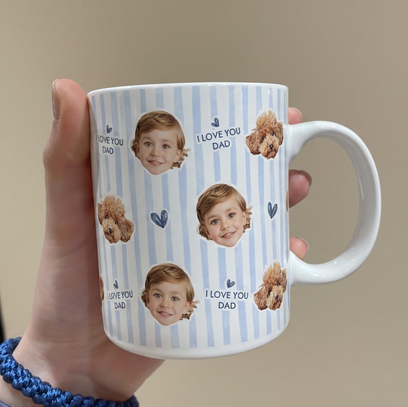 May include: White ceramic mug with a blue striped pattern. The mug features images of a child and a dog, along with the text "I LOVE YOU DAD". A blue woven bracelet is visible in the foreground.