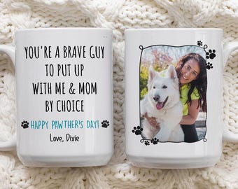 May include: White ceramic mug with the text "YOU'RE A BRAVE GUY TO PUT UP WITH ME & MOM BY CHOICE" and "HAPPY PAWTHER'S DAY! Love, Dixie". The other side features a photo of a woman and a white dog, framed with paw prints.