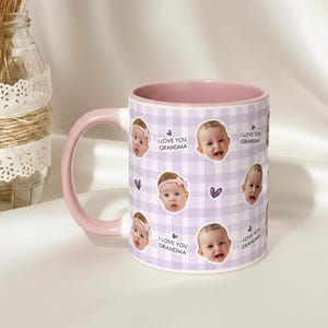May include: A ceramic mug with a pink handle and interior. The mug features a repeating pattern of baby faces, purple hearts, and the text "I LOVE YOU GRANDMA" on a light purple gingham background. A decorative glass jar is in the background.