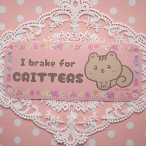 May include: Pink and brown sticker with a cartoon squirrel and the text "I brake for critters".