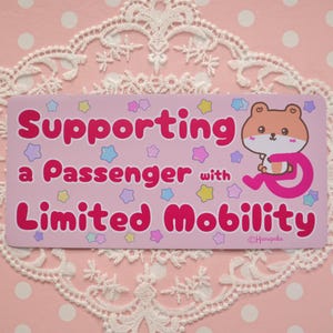 以下が含まれることがあります： ピンク色の長方形ステッカー。太字のピンク色で「Supporting a Passenger with Limited Mobility」と書かれています。右側にはピンク色の車椅子に乗った漫画のハムスターがいます。パステルカラーの星がテキストを囲んでいます。