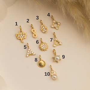 May include: Ten gold-toned charms with clear crystal accents. The charms include a maple leaf, infinity symbol, hamsa hand, star, triangle, sun, seashell, pearl, and two other star-shaped charms.