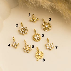 May include: Eight gold-tone charms with clear crystal accents. The charms include a leaf, a snowflake, a flower, a four-leaf clover, and three different star shapes.