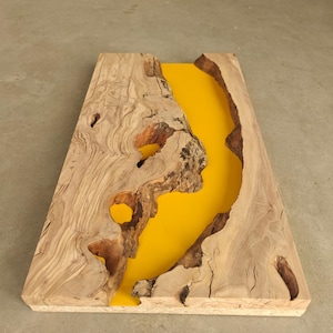 Peut inclure: Table en bois rectangulaire avec une rivière en résine jaune vif au centre. Le bois est de couleur marron clair avec des veines et des nœuds visibles. La table mesure environ 76 cm de long.
